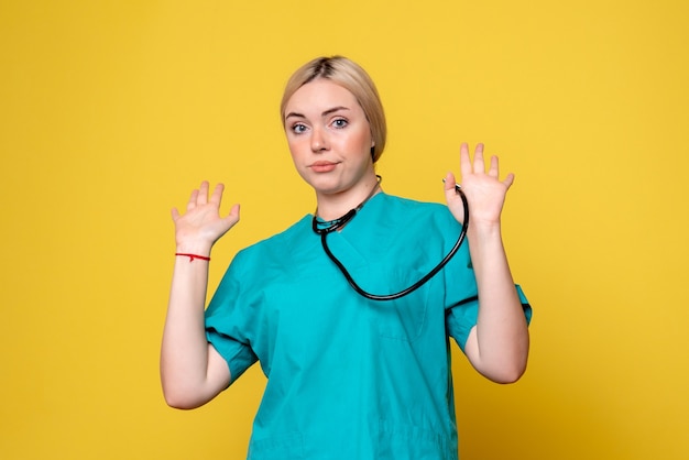 Front view of female doctor in medical shirt with stethoscope on yellow wall