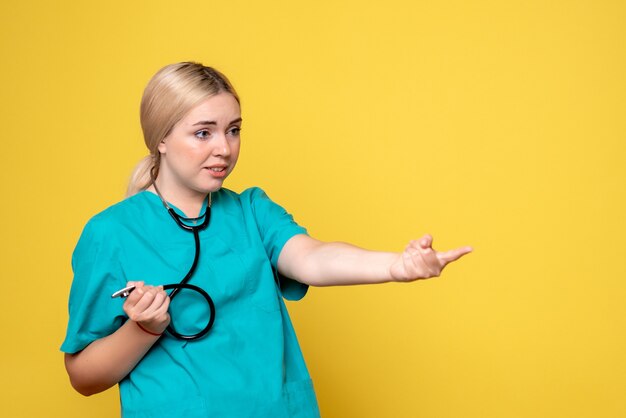 노란색 벽에 청진 기 의료 셔츠에 여성 의사의 전면보기