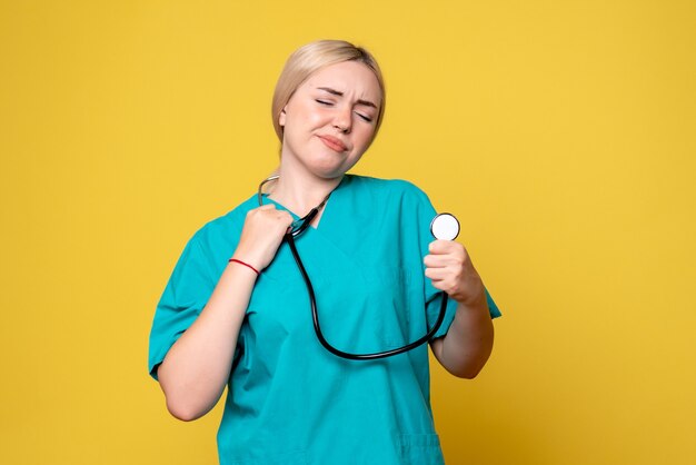 Front view of female doctor in medical shirt with stethoscope on yellow wall