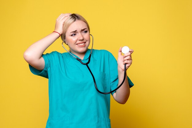 Front view of female doctor in medical shirt with stethoscope on yellow wall