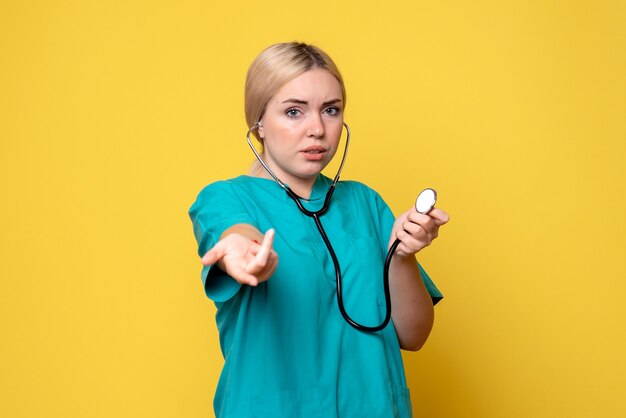 Front view of female doctor in medical shirt with stethoscope on yellow wall