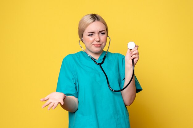 黄色の壁に聴診器と医療シャツの女性医師の正面図