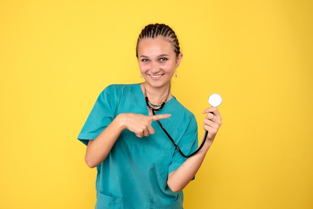 Front view of female doctor in medical shirt with stethoscope on yellow wall