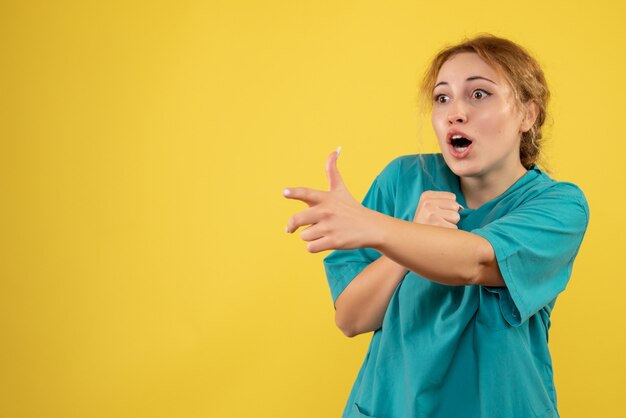 Front view female doctor in medical shirt on yellow desk nurse medic covid-19 color health emotion