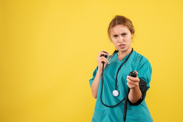 Vista frontale della dottoressa in tuta medica controllando la sua pressione sulla parete gialla