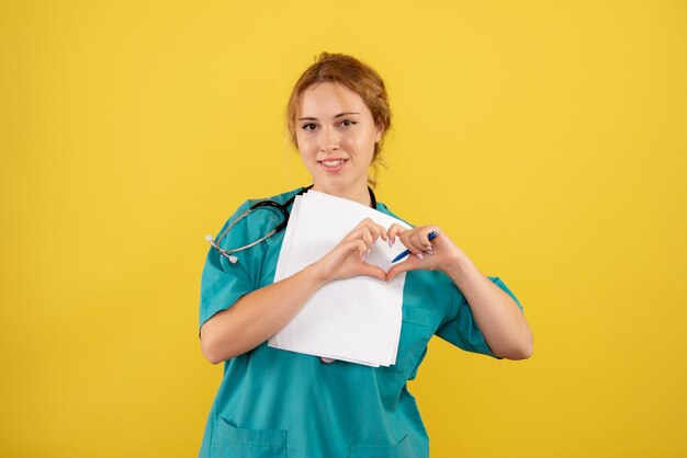 Front view of female doctor in medical suit holding analysis on the yellow wall