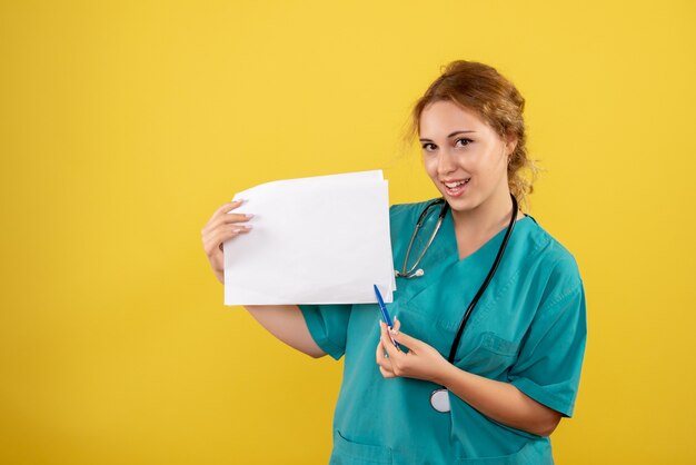 Front view of female doctor in medical suit holding analysis on the yellow wall