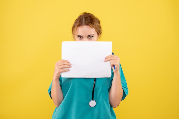 Front view of female doctor in medical suit holding analysis on yellow wall