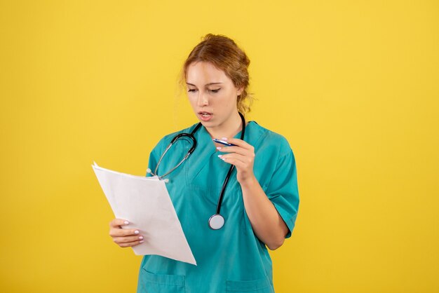 Front view of female doctor in medical suit holding analysis on yellow wall