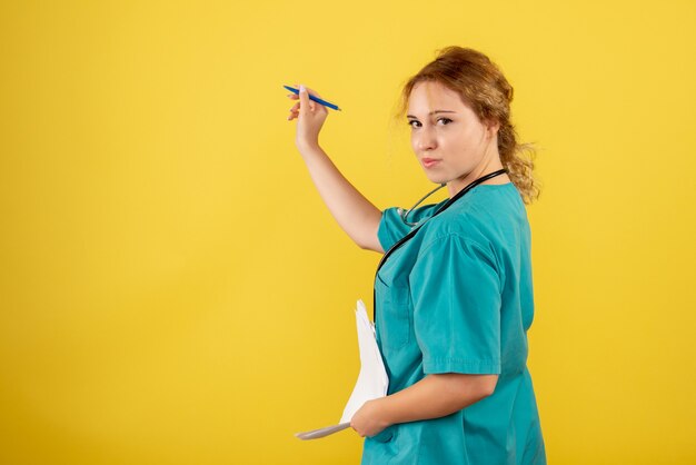 Front view of female doctor in medical suit holding analysis on yellow wall