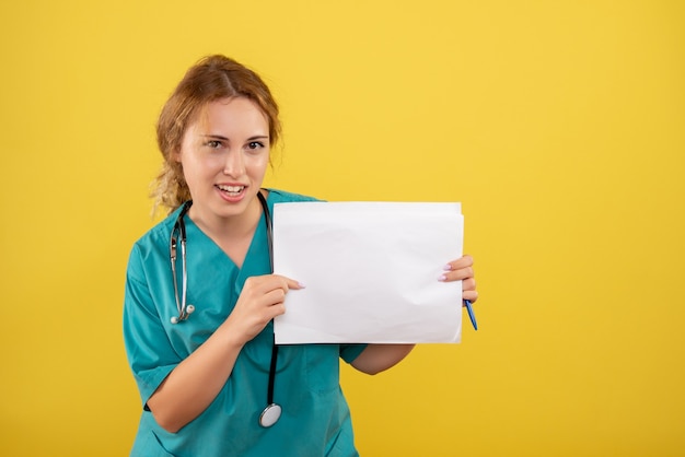 Front view of female doctor in medical suit holding analysis on yellow wall