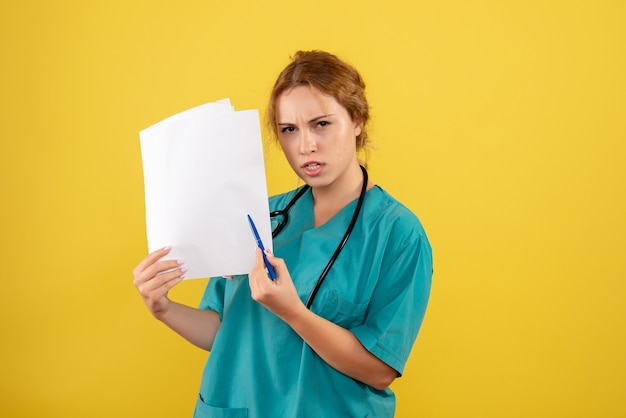 Front view of female doctor in medical suit holding analysis on yellow wall