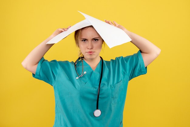 Front view of female doctor in medical suit holding analysis on yellow wall