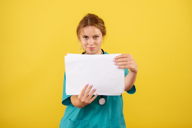 Front view of female doctor in medical suit holding analysis on yellow wall