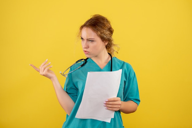 Front view of female doctor in medical suit holding analysis on yellow wall