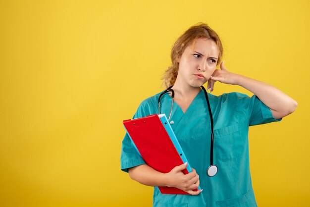 Front view of female doctor in medical suit holding different analysis on yellow wall