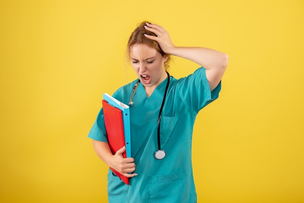 Free photo front view of female doctor in medical suit holding different analysis on yellow wall