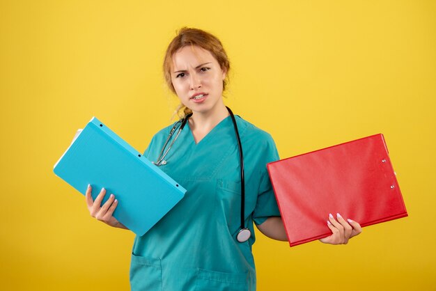 Front view of female doctor in medical suit holding different analysis on yellow wall