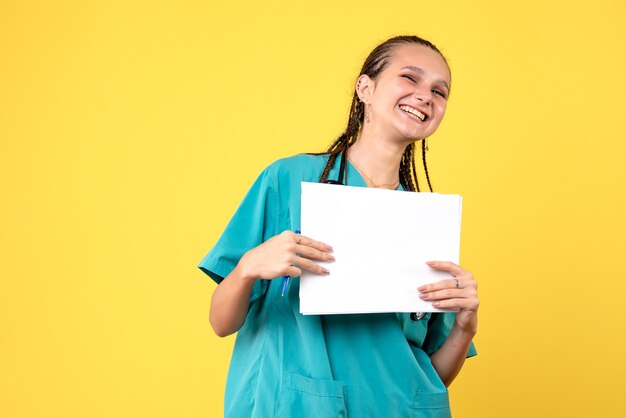 Front view of female doctor in medical suit holding papers on yellow wall