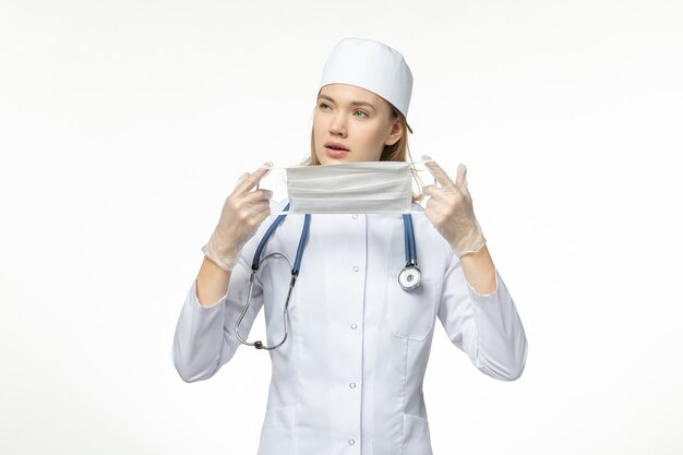 Front view female doctor in medical suit holding protective mask due to coronavirus on white wall pandemic covid- virus illness