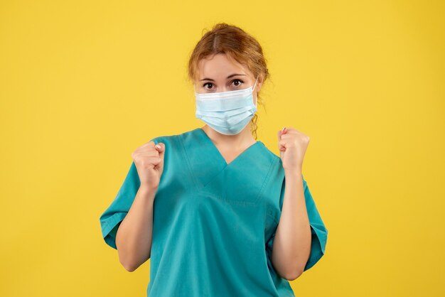 Front view of female doctor in medical suit and mask on a yellow wall