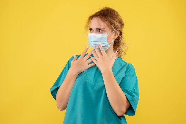 Front view of female doctor in medical suit and mask on a yellow wall