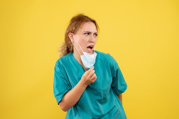 Front view of female doctor in medical suit and mask on a yellow wall