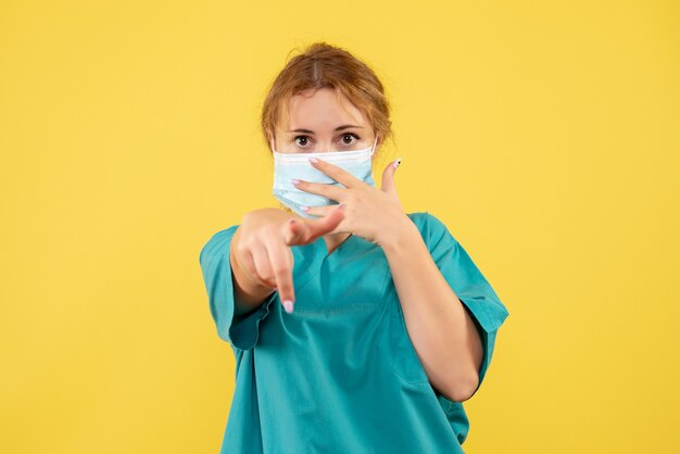 Front view of female doctor in medical suit and mask on yellow wall