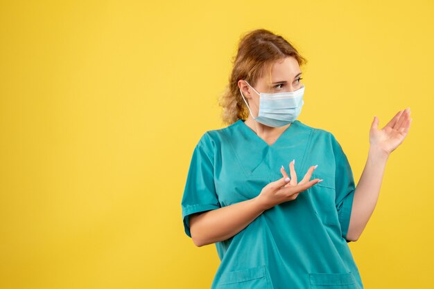 Front view of female doctor in medical suit and mask on yellow wall