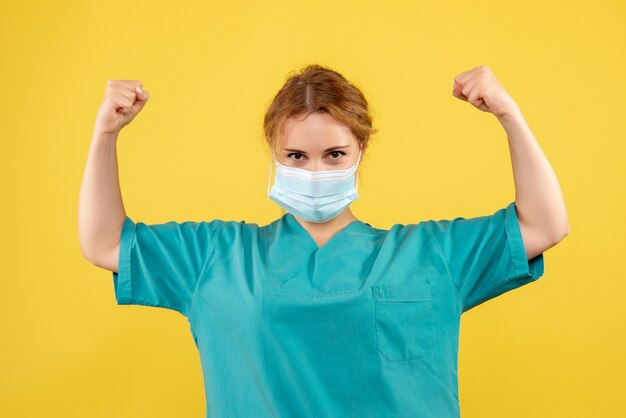 Front view of female doctor in medical suit and mask on yellow wall