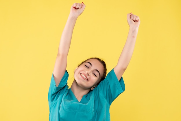 Vista frontale della dottoressa in tuta medica che si rallegra sulla parete gialla