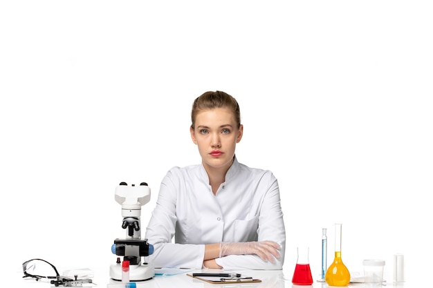 Вид спереди женщина-врач в медицинском костюме, сидящая с решениями на белом пространстве