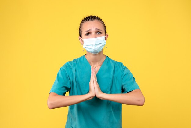 Front view of female doctor in medical suit and sterile mask on yellow wall