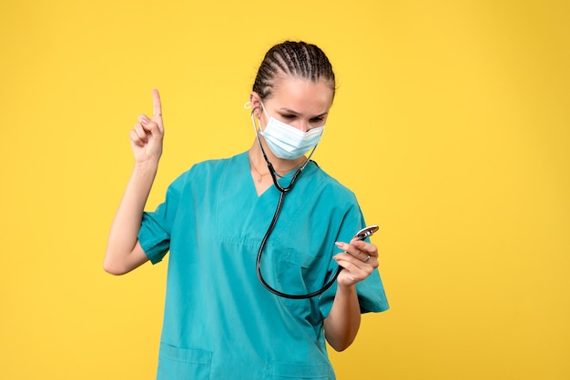 Front view of female doctor in medical suit and sterile mask on yellow wall