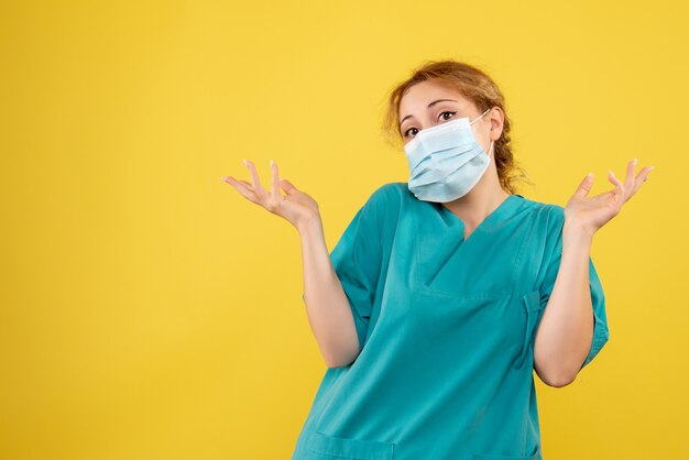 Front view of female doctor in medical suit and sterile mask on yellow wall