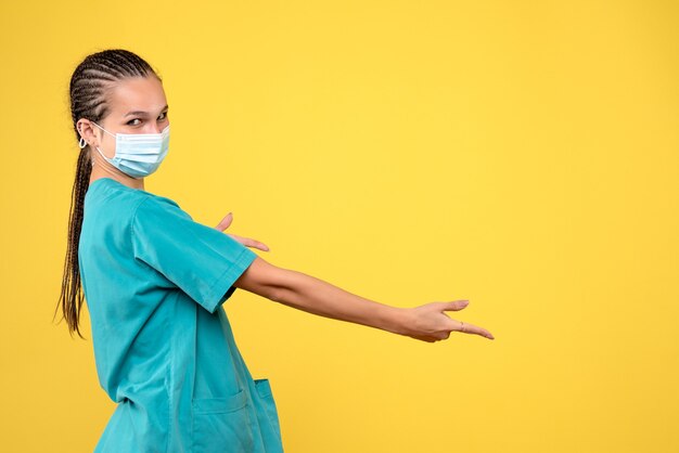 Front view of female doctor in medical suit and sterile mask on yellow wall