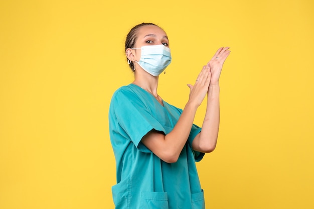Front view of female doctor in medical suit and sterile mask on yellow wall