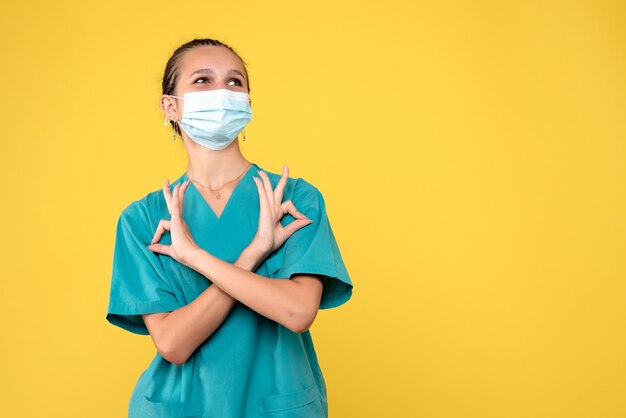 Front view of female doctor in medical suit and sterile mask on yellow wall