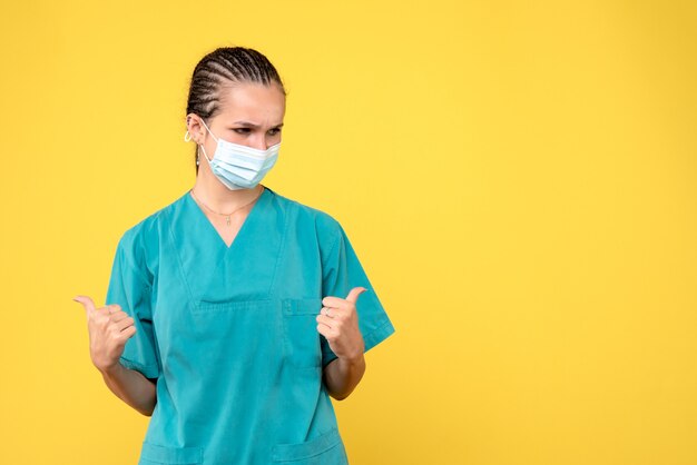 Front view of female doctor in medical suit and sterile mask on yellow wall