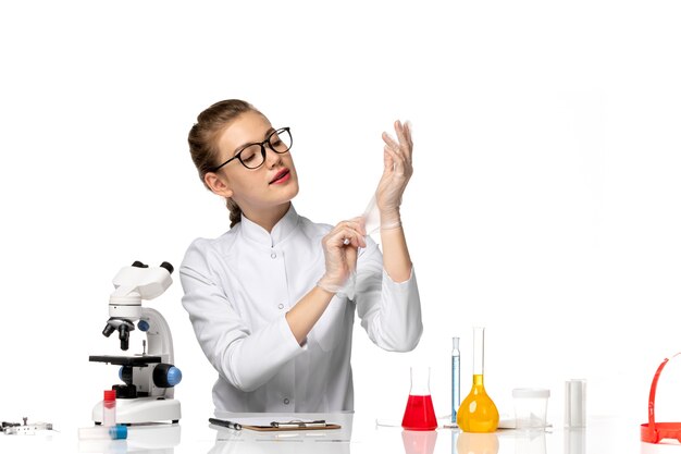 Front view female doctor in medical suit wearing gloves due to covid on white space