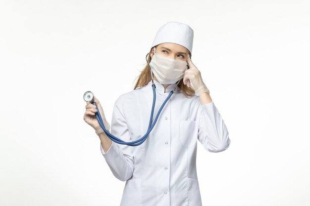 흰 벽 바이러스 유행성 covid- 질병에 대한 청진 생각을 들고 코로나 바이러스로 인해 마스크를 착용하는 의료 소송에서 전면보기 여성 의사