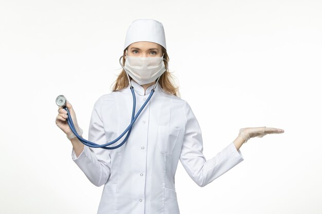 흰색 바닥 바이러스 유행성 covid- 질병에 청진기를 들고 코로나 바이러스로 인해 마스크를 착용하는 의료 소송에서 전면보기 여성 의사