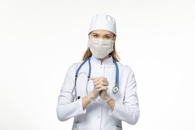 Front view female doctor in medical suit wearing mask due to coronavirus on light-white desk disease covid- pandemic virus illness