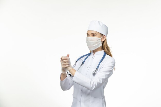 Front view female doctor in medical suit wearing mask due to coronavirus on the light white desk disease covid- pandemic virus illness