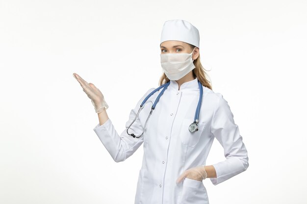 Front view female doctor in medical suit wearing mask due to coronavirus on light white wall disease covid- pandemic virus disease illness