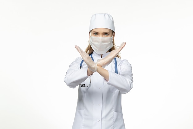 Front view female doctor in medical suit wearing mask due to coronavirus showing ban sign on white wall disease covid- pandemic virus disease illness