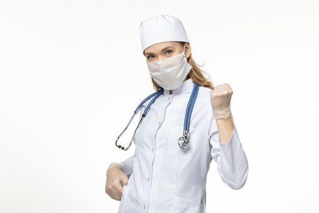 Front view female doctor in medical suit wearing mask due to coronavirus on white desk disease virus covid- pandemic disease illness