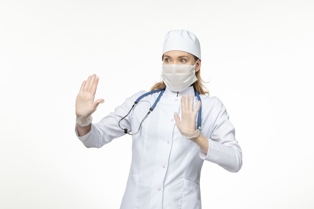 Front view female doctor in medical suit wearing mask due to coronavirus on the white wall disease virus covid- pandemic disease illness