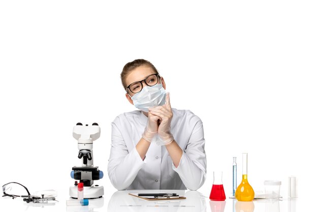 Front view female doctor in medical suit wearing mask due to covid on light-white space