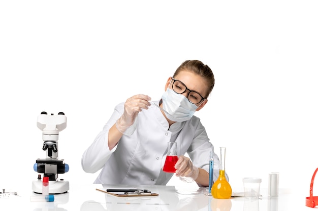 Front view female doctor in medical suit wearing mask due to covid working with solutions on the white space